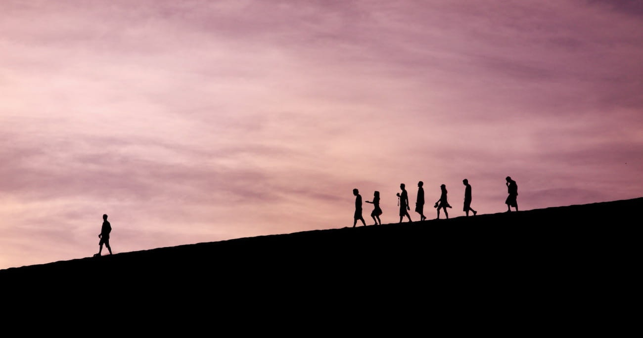 silhouette of people walking on a hill with one leading the way