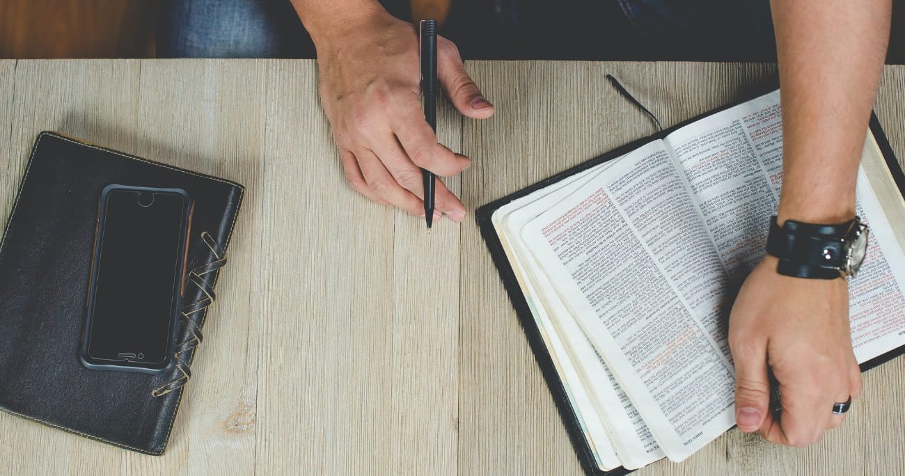 overhead view of a Bible and a man holding a pen