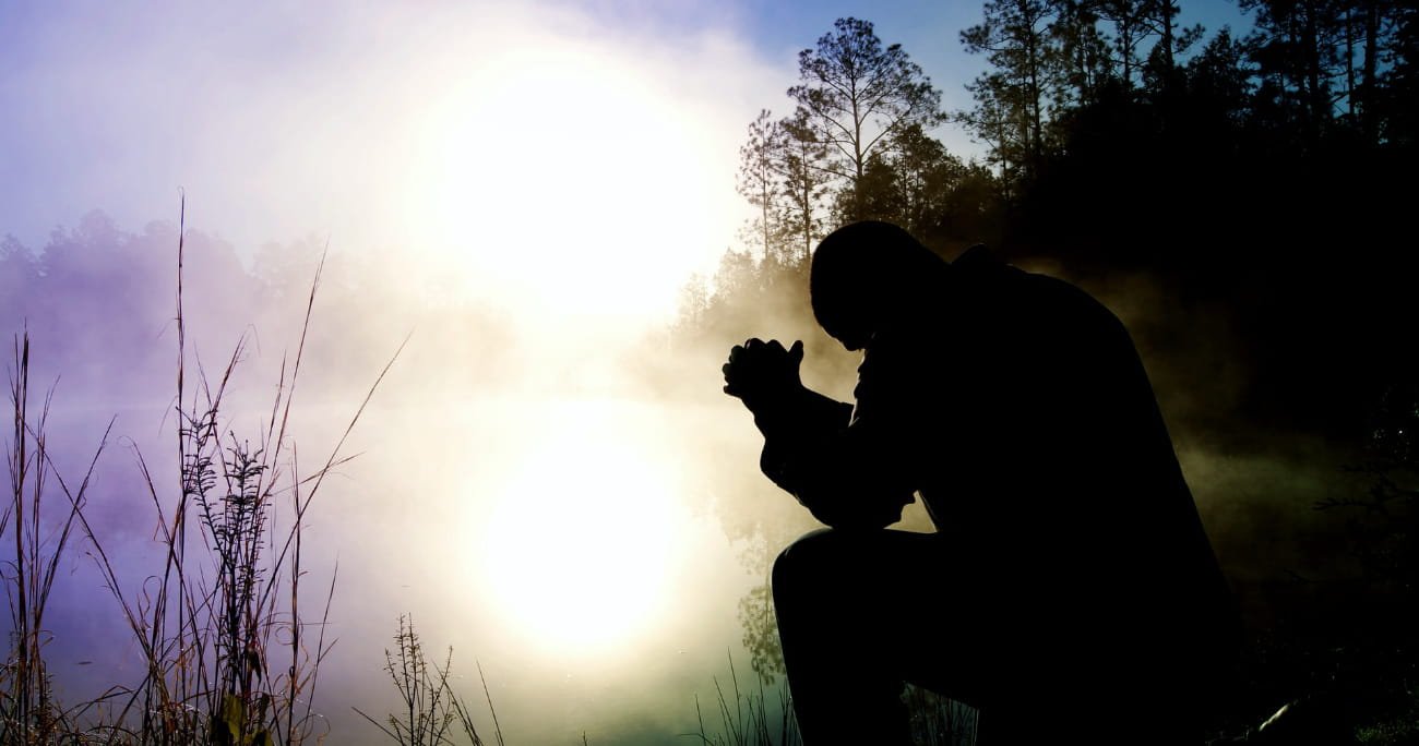 man kneeling in prayer outside