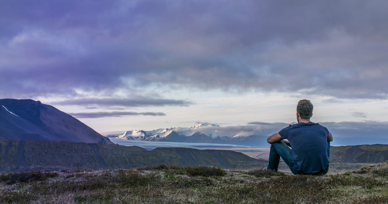 man facing away from the camera sitting down and looking over a mountain range