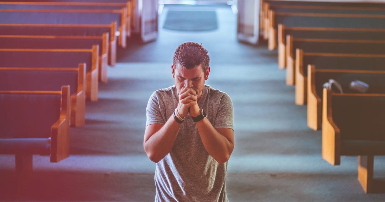 man kneeling in prayer in the front of a church