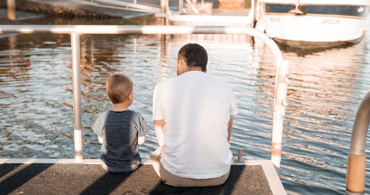 dad and child sitting on dock and looking out over a lake